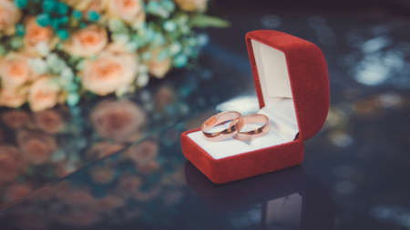 Wedding gold wedding rings on the background of a bouquet of peach roses in a red box close-up