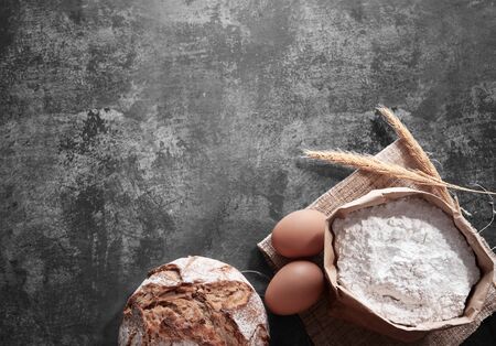Homemade bread with wheat ears, eggs and bag of flour on gray background. Top viewの写真素材