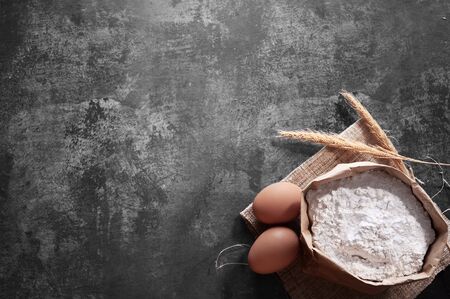 Bread ingredients with wheat ears, eggs and bag of flour on gray background. Top viewの写真素材