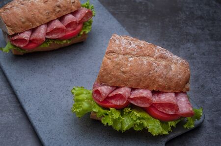 Breakfast sandwiches with salami, tomato, lettuce on gray board as backgroundの写真素材