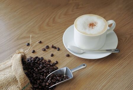 Coffee beans roasted in bag and cappuccino on a wooden background in the morning.の写真素材