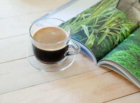 Fresh coffee in glass on wooden table with magazing in the morningの写真素材