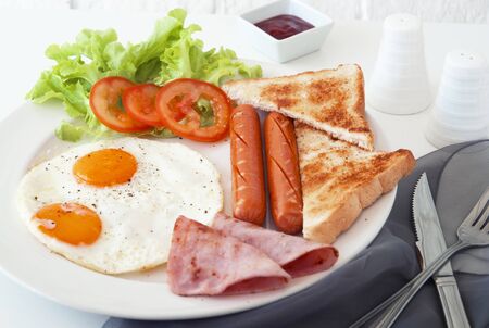Morning breakfast, Fried egg, sausage and ham in white dish on table together light in the morningの写真素材