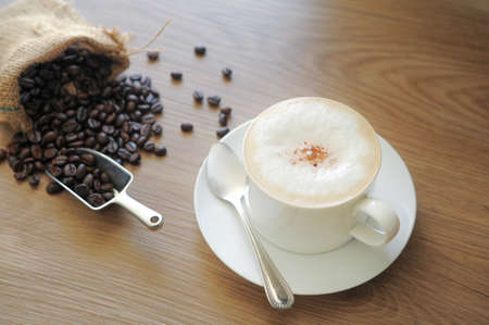 Coffee cup of Cappuccino and Coffee beans roasted in bag on a wooden background in the morning.の写真素材