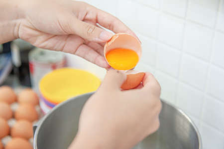 Woman hands to egg shells and separate egg yolk for made bakery ingredient and cooking.の写真素材