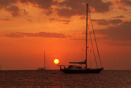 Sailboat stop on the sea at sunset and two sailboat against a vivid colorful sunset.の写真素材