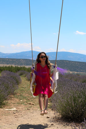 Woman swinging on the swing in the middle of the lavender field under the skyの写真素材