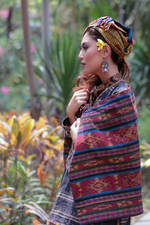 Portrait of beautiful Asian Woman in traditional Indonesian clothing complete with assorted accessories posing against a green park in the background.のeditorial素材