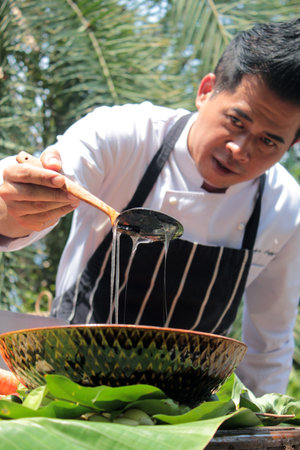 Hands of Thai chef pouring coconut oil in a bowl with banana leafのeditorial素材