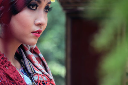Close-up of a beautiful Asian model dressed in modern batik with a distinctive Lombok pattern, smiling looking to the side with red lips and curled eyelashes.のeditorial素材