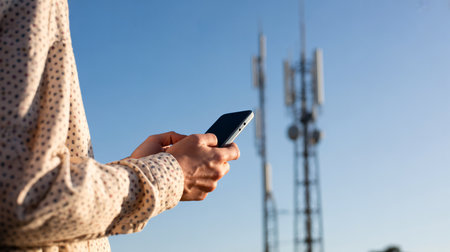Close-up of woman using mobile phone with cell phone tower in the backgroundの素材