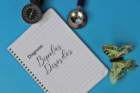 Layout of Stethoscope, note book and fake butterfly with the text DIAGNOSE: BIPOLAR DISORDER on blue backgroundの写真素材