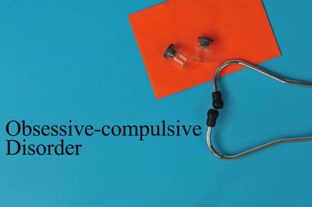 Layout of Stethoscope, orange paper and glass vials with the text OBSESSIVE-COMPULSIVE DISORDER on blue backgroundの写真素材