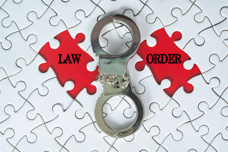 Business concept. Handcuff and jigsaw puzzle with text law and order on red background. Selective...