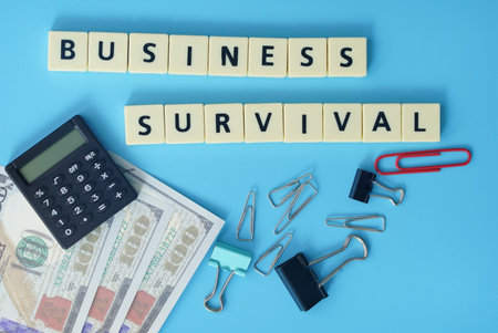 Business concept. Layout of fake money, calculator, paper clips and text business survivalの写真素材
