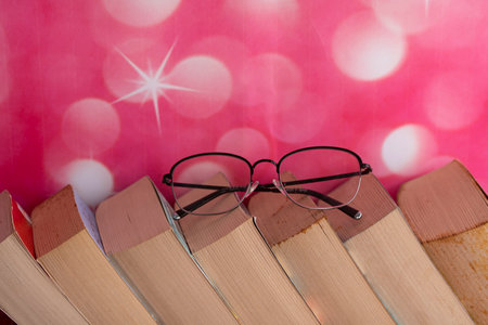 Close-up of a stack of books arranged slanted side by side with reading glasses. Selective focus points. Blurred backgroundの写真素材