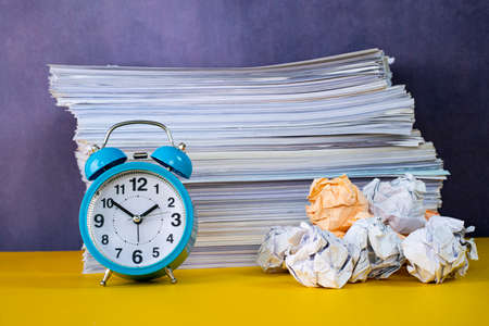 Business concept. Layout of alarm clock, stack of papers and crumpled papers depicting procrastinateの写真素材