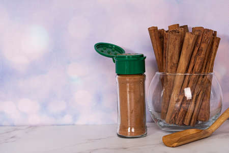 Some cinnamon sticks in a glass bowl and a bottle of cinnamon powder with wooden spatula. Selective focus points. Blurred backgroundの写真素材