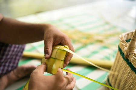 Weaving the coconut leaves making the ketupat, a traditional Malay cuisine during the Eid...