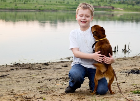Boy play on the lake bank with dog - petit brabancon.の写真素材