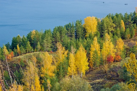 Excellent autumn landscape with yellow, red and green leaves on the trees. The tree line down to the blue river. In the river, the fishermen are fishing from boats.の写真素材