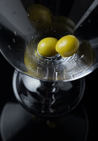 Two green olives waiting when alcohol will fill the glass. Help them.の写真素材