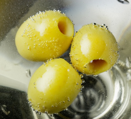 Macro photo of three green olives in a cocktail glass. Olives floating in carbonated alcohol - champagne wine.の写真素材
