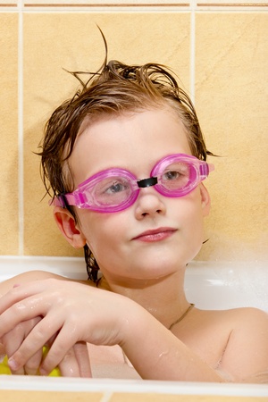 Cute boy have fun in the bathroom. The boy in the foam bath and swimming goggles.の写真素材