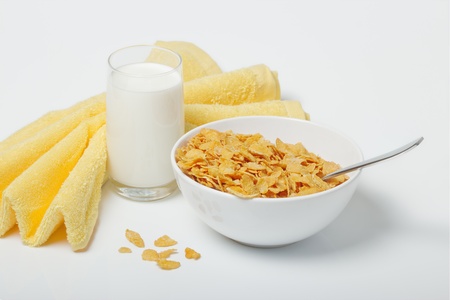 Corn flakes in deep plate with spoon, glass with milk and yellow towel.