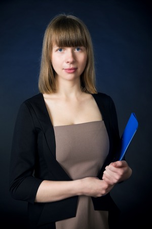 Woman with folder in casual business suit stand over dark blue background.の写真素材