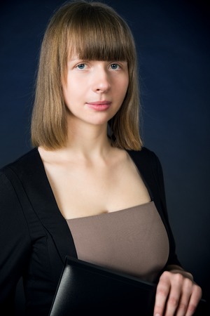 Woman with folder in casual business suit stand over dark blue background.の写真素材