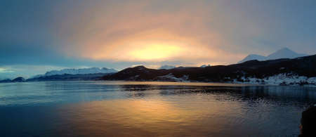 Sunset on a frozen lake with mountains in the backgroundの写真素材