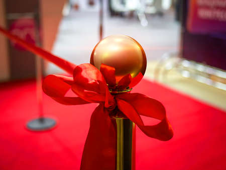 Opening ceremony of an event. A red festive satin ribbon tied to a gold post. Ribbon cutting ceremony. Red carpet for visitorsの写真素材