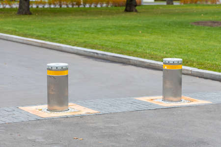 Two automatic security bollards on the asphalt road. Pillars for safe movement. Bollards with...