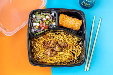 Food delivery at home concept. Greek salad with onions, roll California and noodles with pork. Orange and blue background divided into halfの写真素材