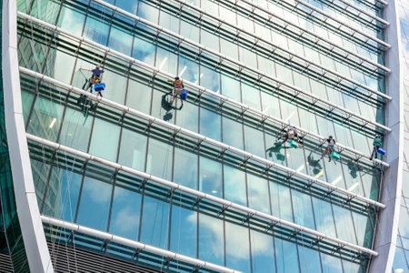4 climbers wash the windows on the facade of a green high-rise office buildingの写真素材