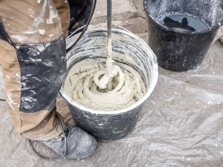 Mixing plaster in a bucket using an electric mixer. Outdoor workの写真素材