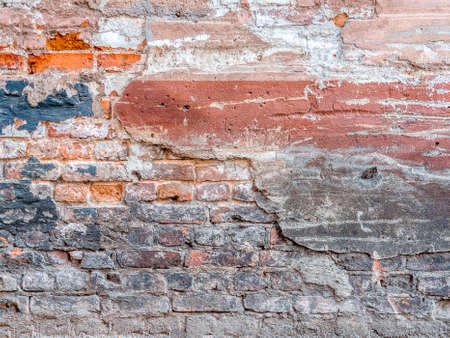 Old mechanically damaged colored stucco collapses from a brick wall. Concept of devastation. Abandoned building needs repairの写真素材