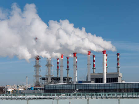 Several chimneys of the heating plant are releasing plumes of steam or white smoke. Heating of residential buildings, offices and enterprises. The work of the city heating plantの写真素材