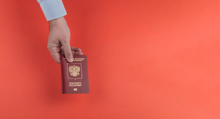 A mans hand holds a Russian passport on a red background. Official state document. Copy spaceの写真素材