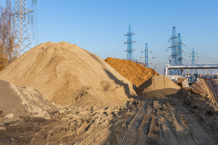Several piles of sand and high voltage poles. Laying a heating main and building a highway. Updating the city engineering infrastructure. Construction site with bulk materialsの写真素材