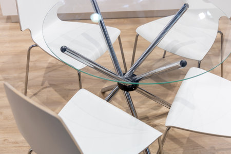 Glass table with metal chrome legs and white chairs around. Modern office furniture for communication between participants of corporate events or company employeesの写真素材