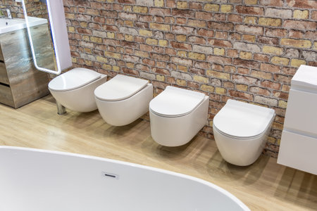 A row of white modern design toilets in a plumbing store. A white toilet is displayed on a stand in a store or at a fair. Toilet equipment. Cleanliness and hygieneの写真素材