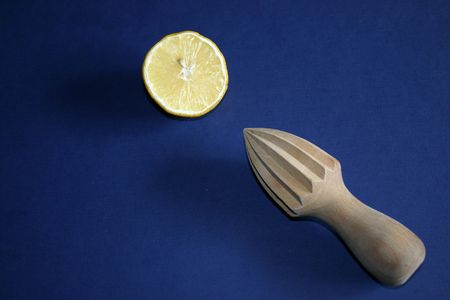 classic wooden lemon squeezer to extract juice from lemon half on a blue background.の写真素材