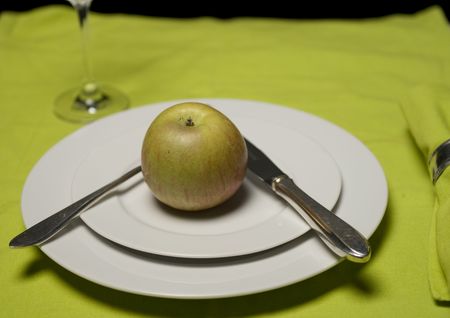 apple on plate with knife and fork and glass on applegreen table clothの写真素材