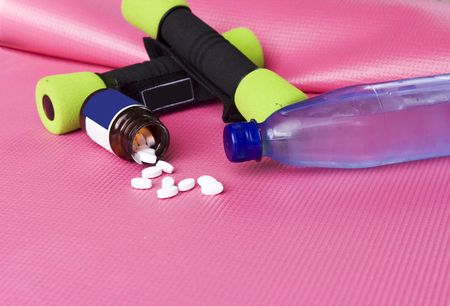 Yellow green dumbbells on a pink excercise mat with vitaminpills and bottle of waterの写真素材