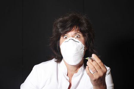 Female doctor with syringe and mouthcap looking scaryの写真素材