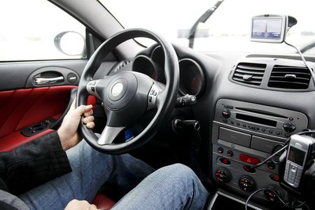 Man behind steering wheel of car with all kinds of equipment like a gps and mobile phoneの写真素材