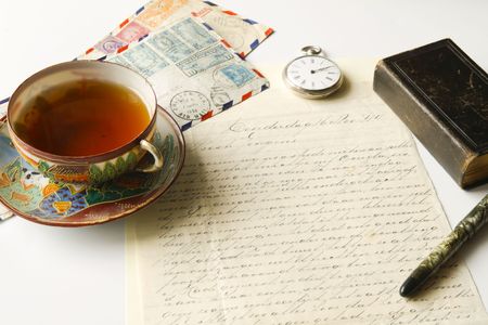 Vintage scene of old handwritten letter, us airmail envelopes, antique fountain pen, pocket watch, chinese porcelain tea cup filled with tea and lold eather pocket bibleの写真素材
