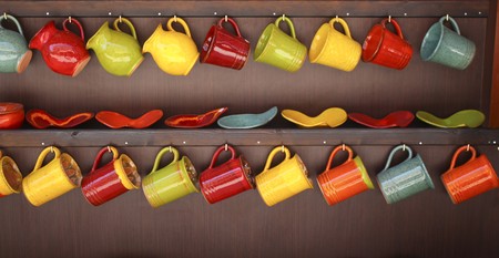 Two rows of colorful  ceramic mugs hanging の写真素材